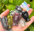 Hand holding various colorful stone carvings against a green leafy background