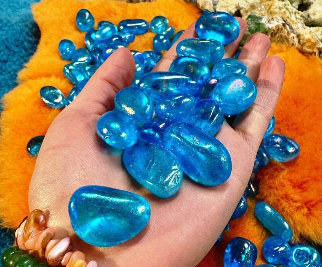 Hand holding blue transparent stones against an orange and green textured background