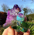 Colorful crystal held in a hand with a blurred outdoor background