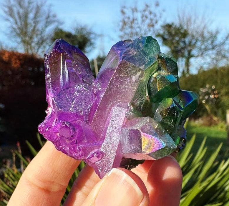 Multicolored crystal held in a hand with a natural outdoor background