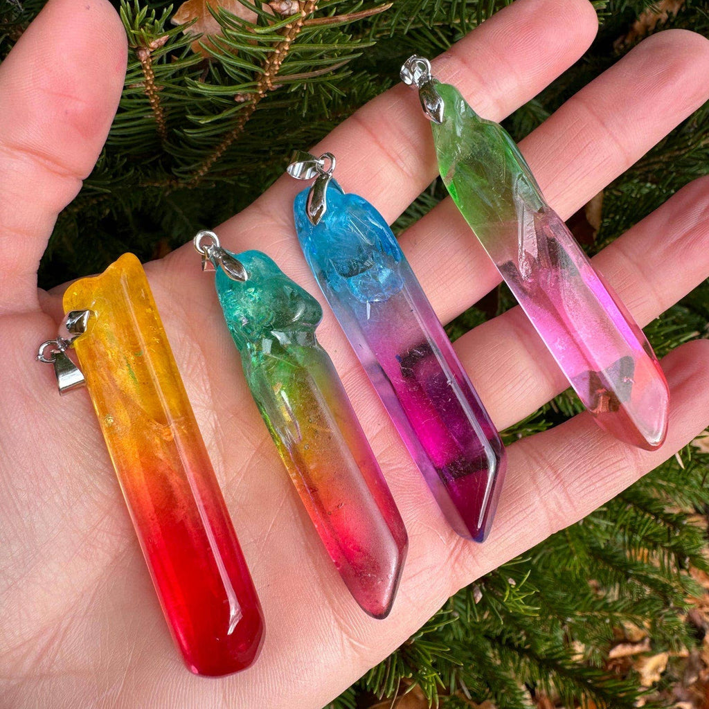 Colorful crystal-like pendants on a hand with a green leafy background
