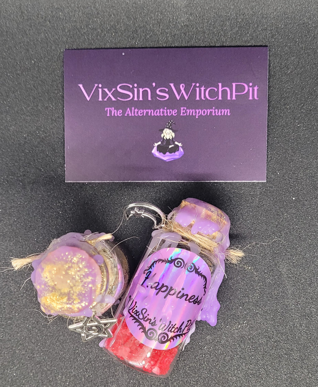 Decorative Spell-bottle with purple label and glittery texture, branded 'VixSin's WitchPit', on a dark background.