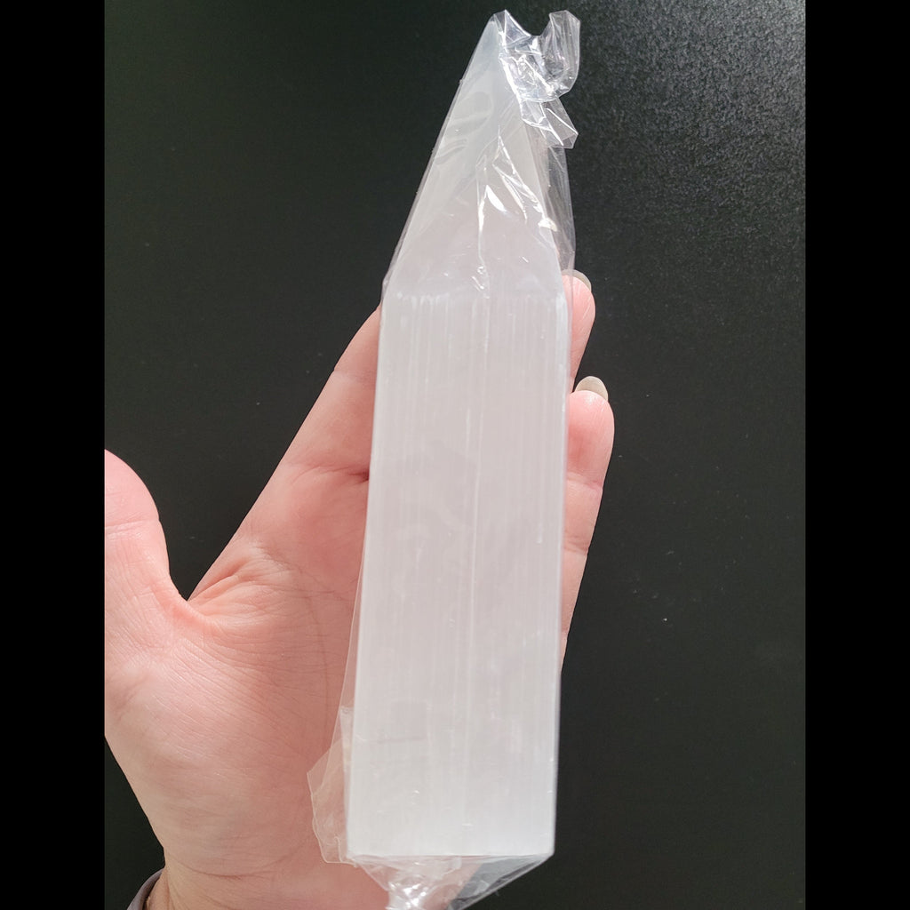 Hand holding a clear Selenite crystal obelisk with a black background
