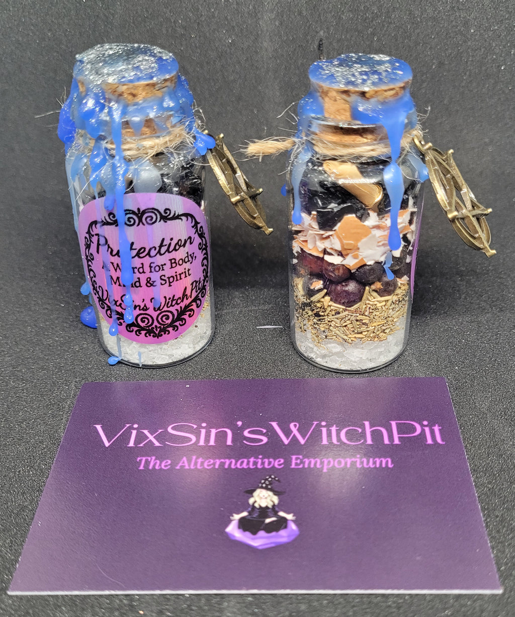 Two small glass Spell jars with decorative elements on a black background, featuring 'VixSin's WitchPit' branding. Protection.